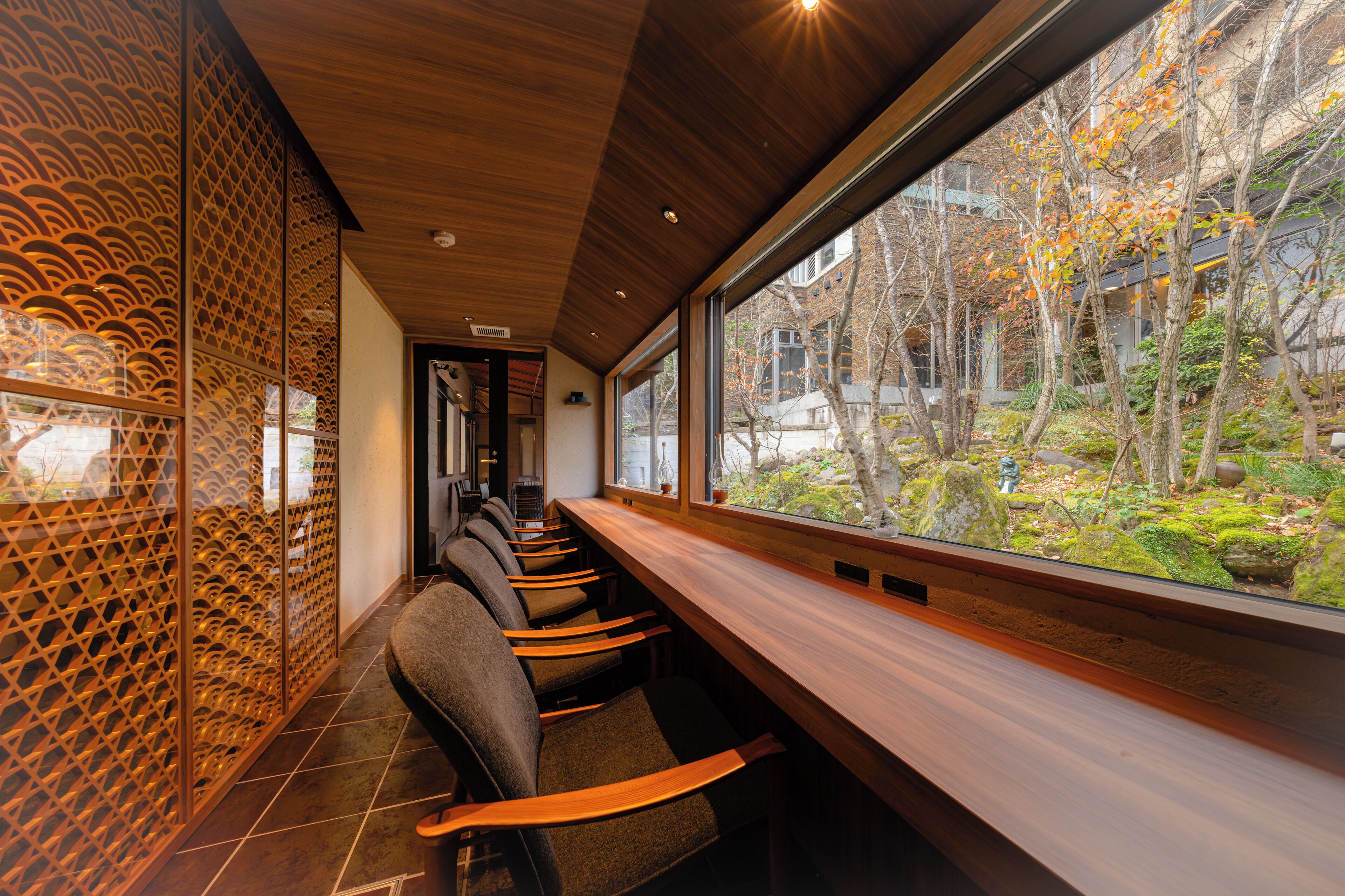 A modern interior with a long wooden bench and a view of a garden through large windows.