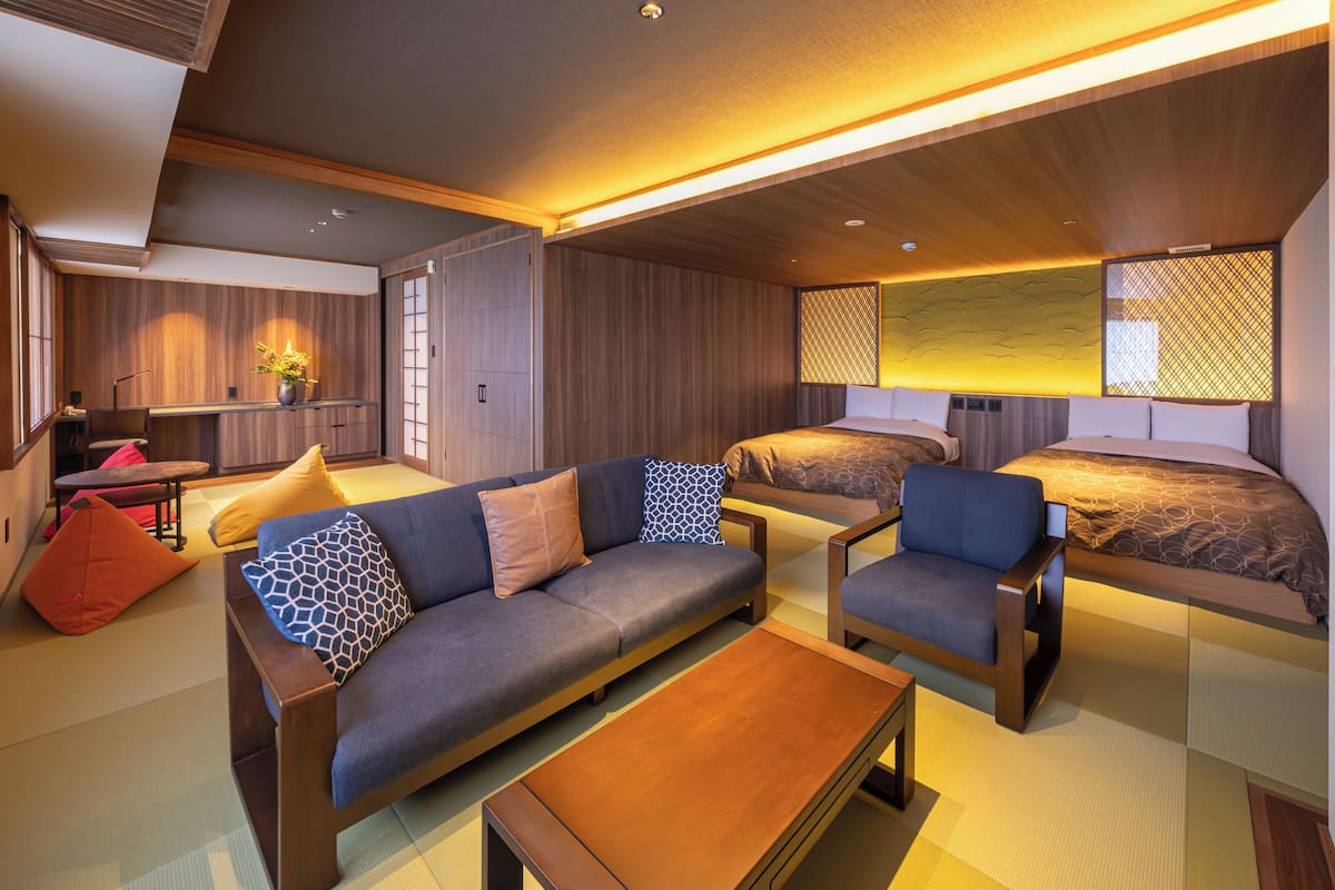 A modern hotel room with a sofa, two single beds, a small table, and a wooden coffee table.