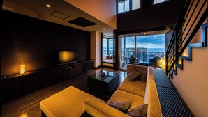 A modern living room with a sofa, a coffee table, and a TV. There is a balcony with a view of the city.