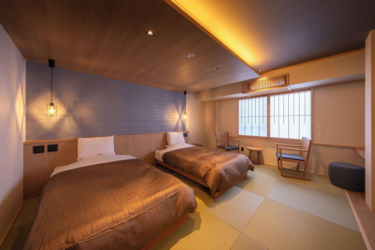 A hotel room with two beds, a small table, and a chair.