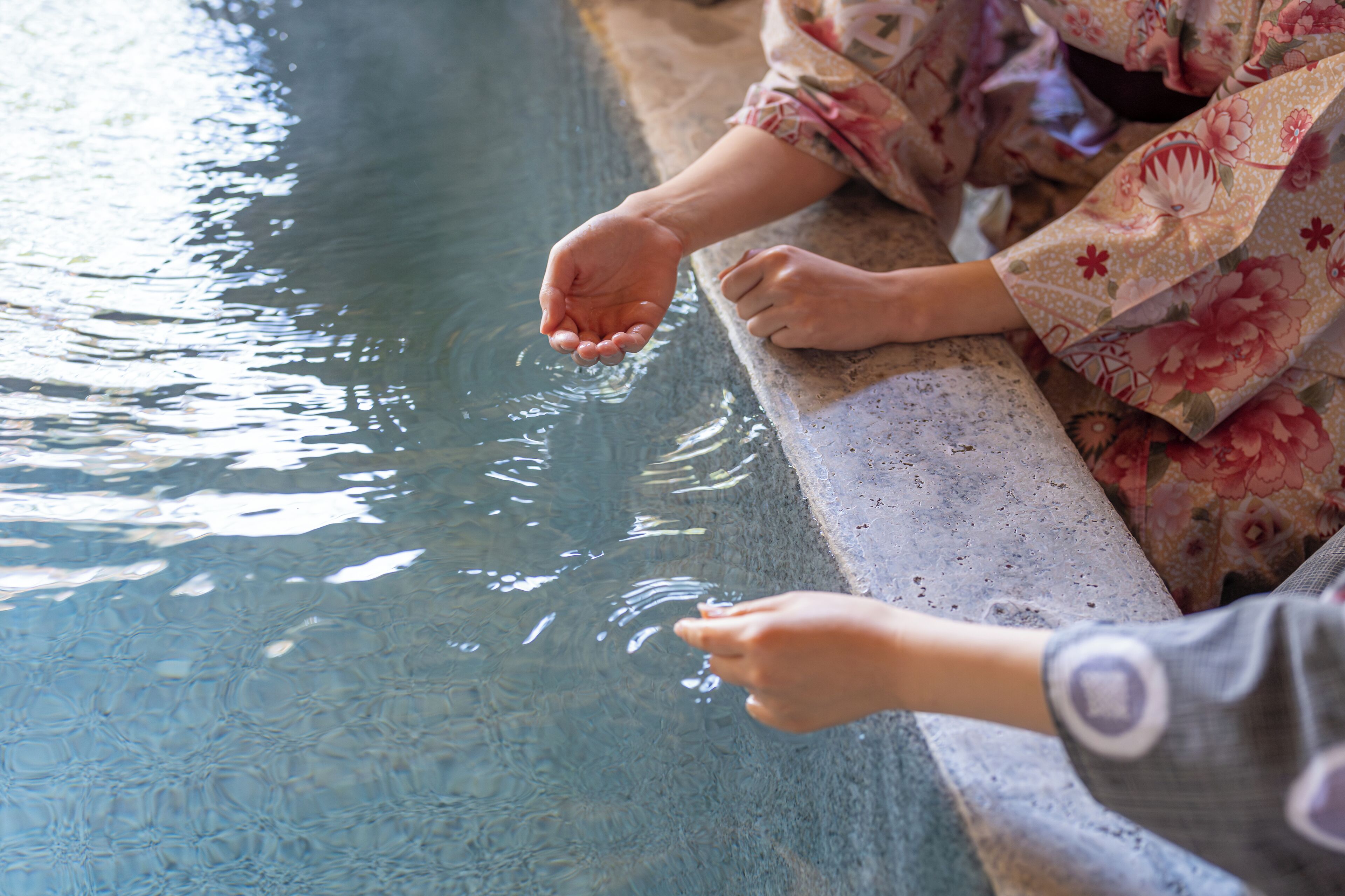 A person in traditional attire by a pool with clear water.