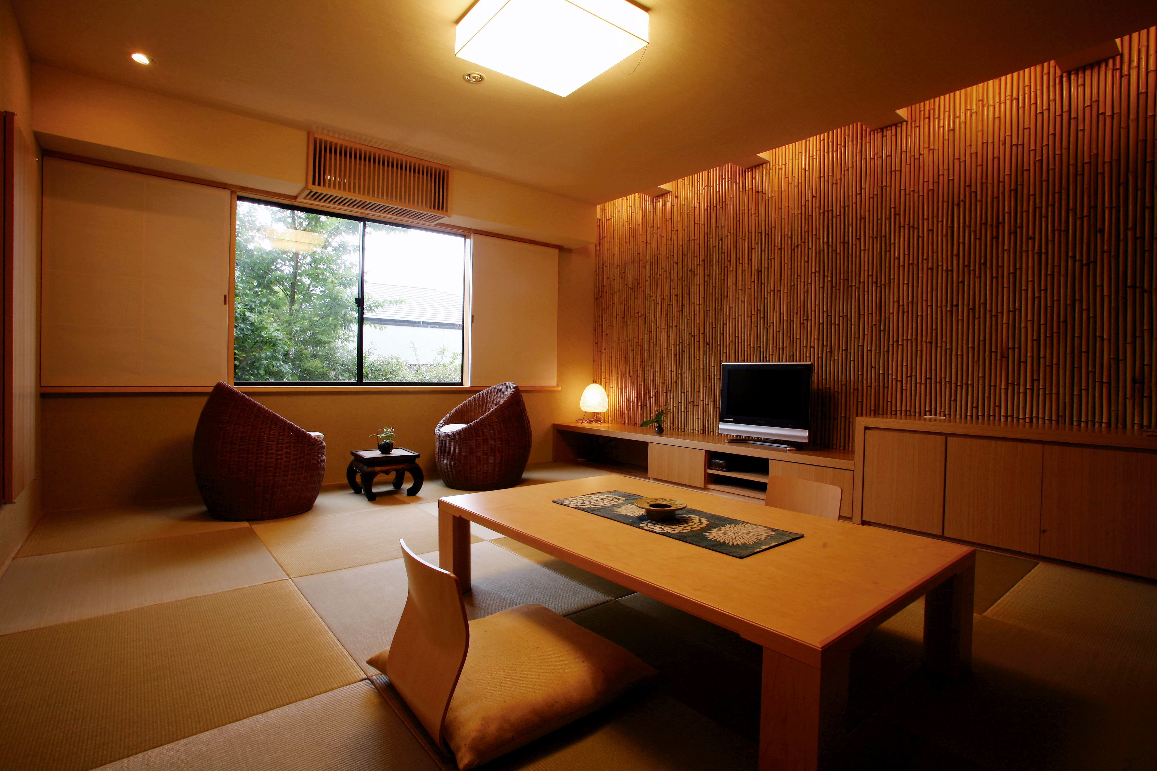 Une pièce de style japonais traditionnel, avec un sol recouvert de tatamis, une table basse, des coussins, un téléviseur et une porte coulissante.
