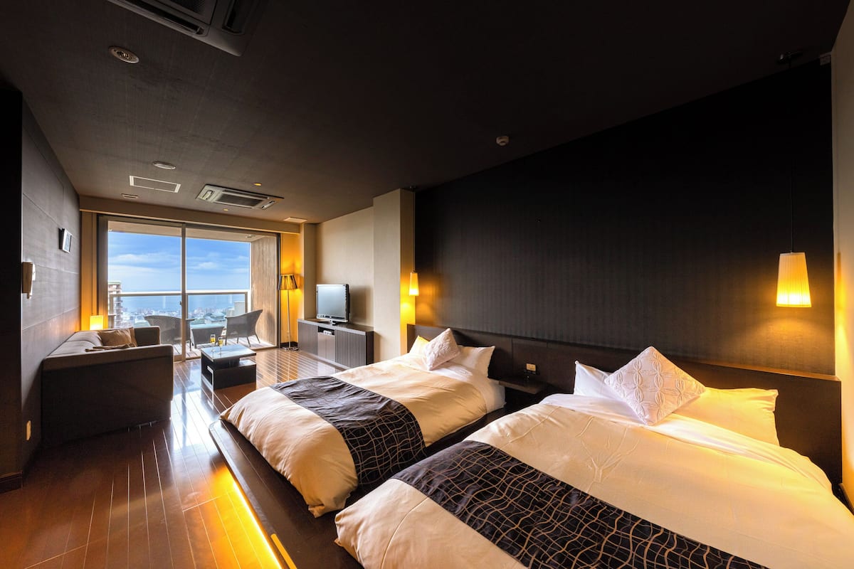 A hotel room with two beds, a sofa, a TV, and a city view.