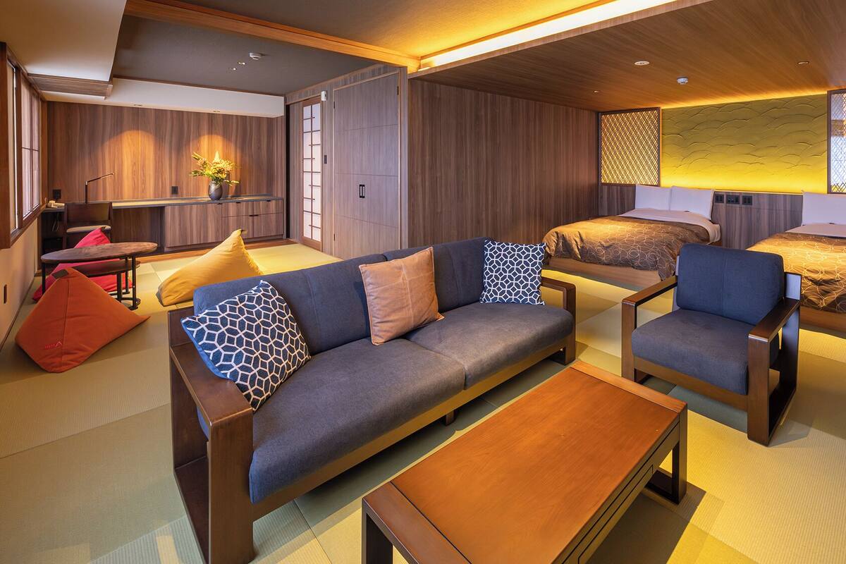 A modern hotel room with a sofa, armchairs, a small table, and a bed.
