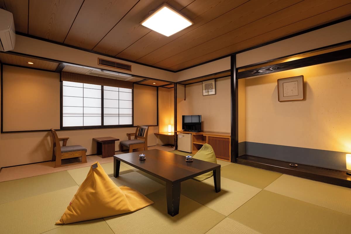 A traditional Japanese room with tatami flooring, a low table, cushions, a television, and sliding doors.