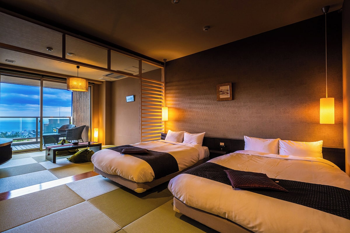A hotel room with two beds, a large window with a city view, a balcony, and a modern design.