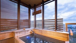 A traditional Japanese onsen with wooden benches and a view of the cityscape through large windows.