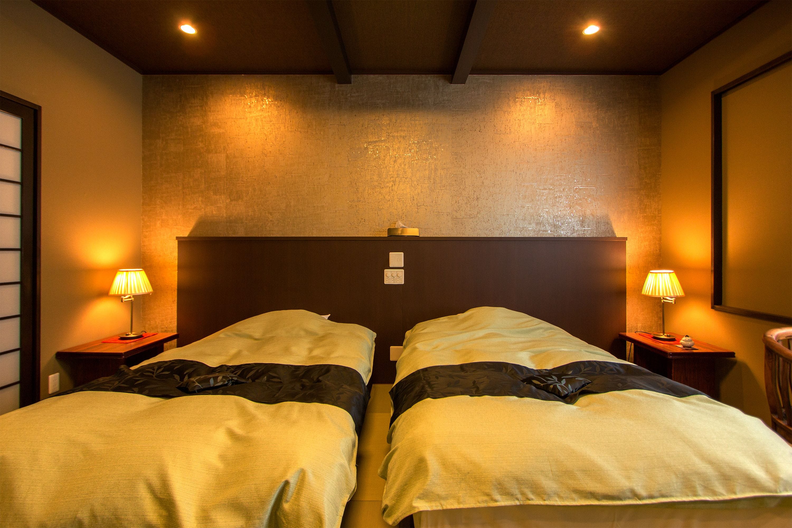 Habitación de hotel con dos camas, cada una con cabecero de madera, dos lámparas de noche y una mesita entre ellas.