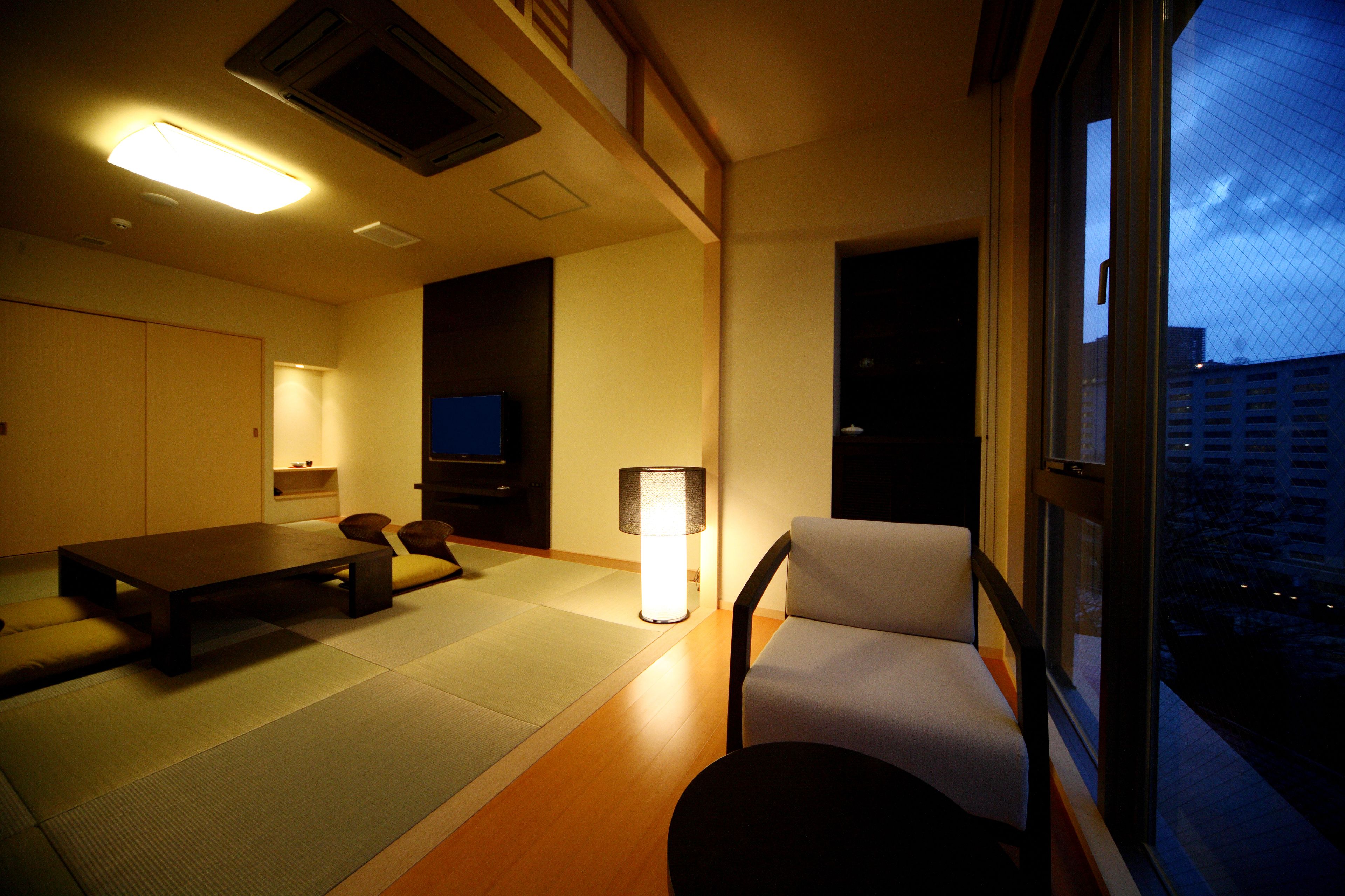 A room with tatami flooring, a low table, a sofa, a chair, and a television.