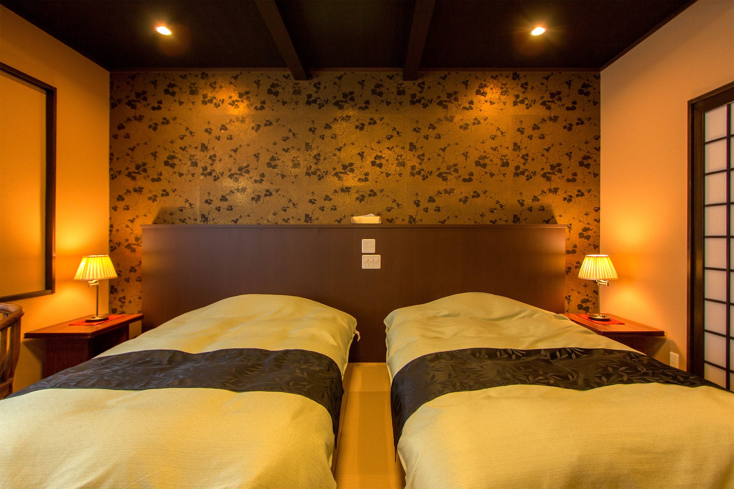A hotel room with two beds, a wooden headboard, floral wallpaper, and bedside lamps.