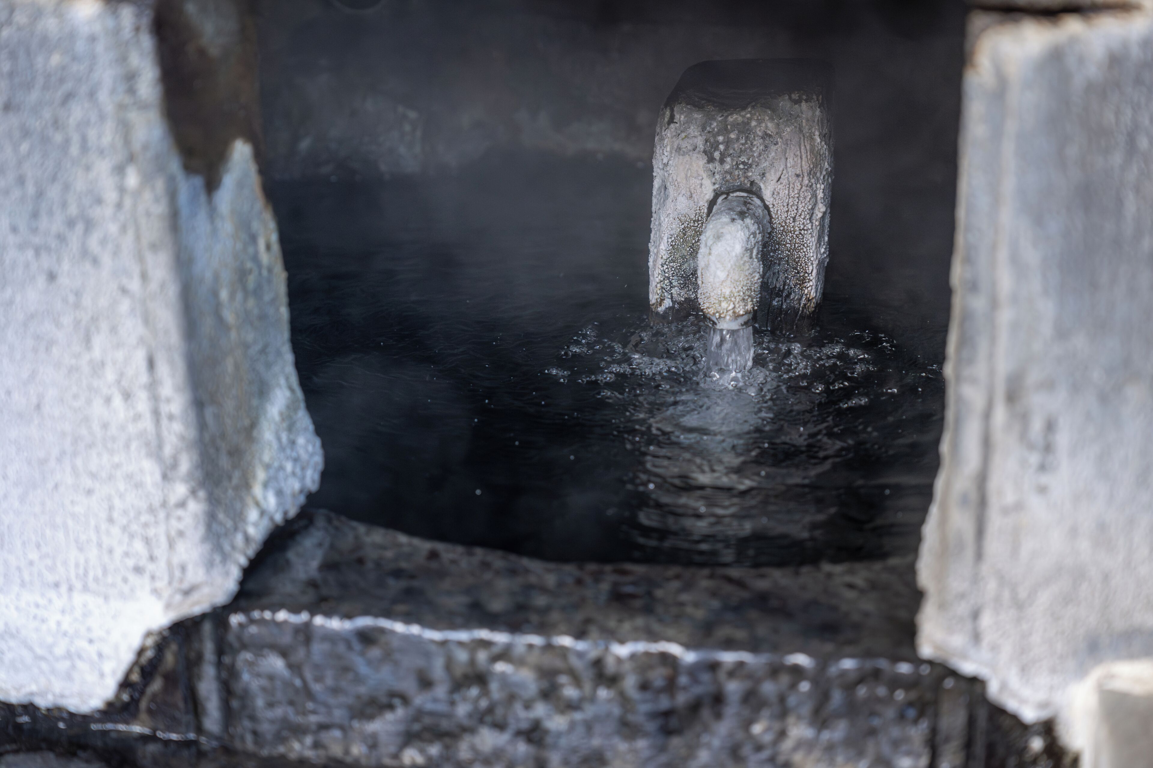 A stone structure with a water spout, surrounded by a rough, textured surface.