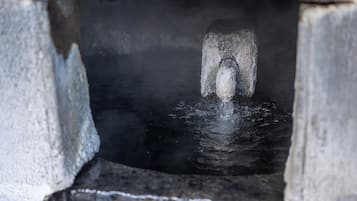 A stone structure with a water spout, surrounded by a rough, textured surface.