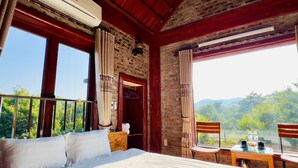 Un dormitorio con una cama grande, una mesa de madera con sillas, un balcón y vistas a zonas verdes y montañas.