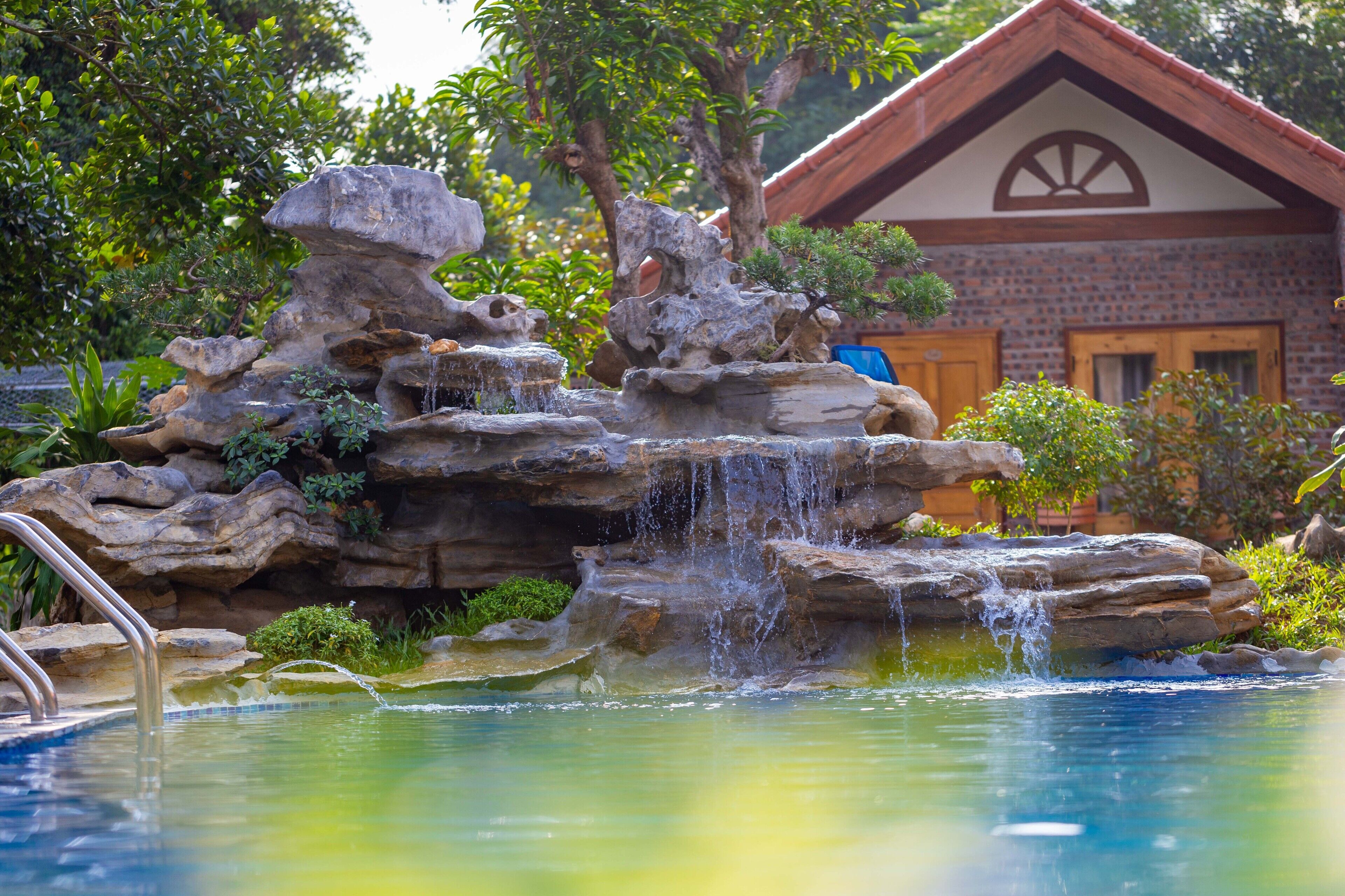 A naturalistic rock formation with a waterfall, surrounded by lush greenery and a pool.