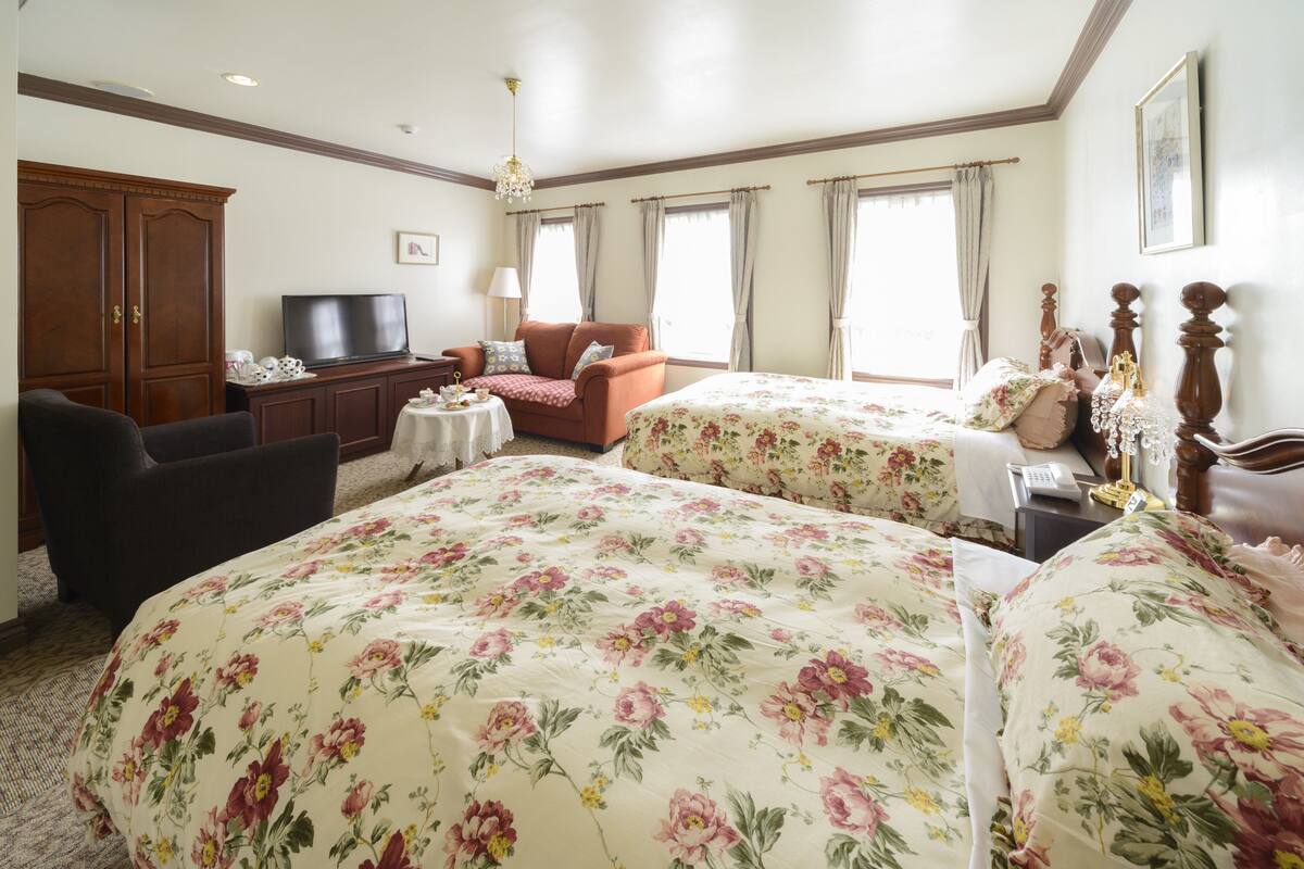 A hotel room with two beds, a TV, a sofa, and a desk with a lamp.