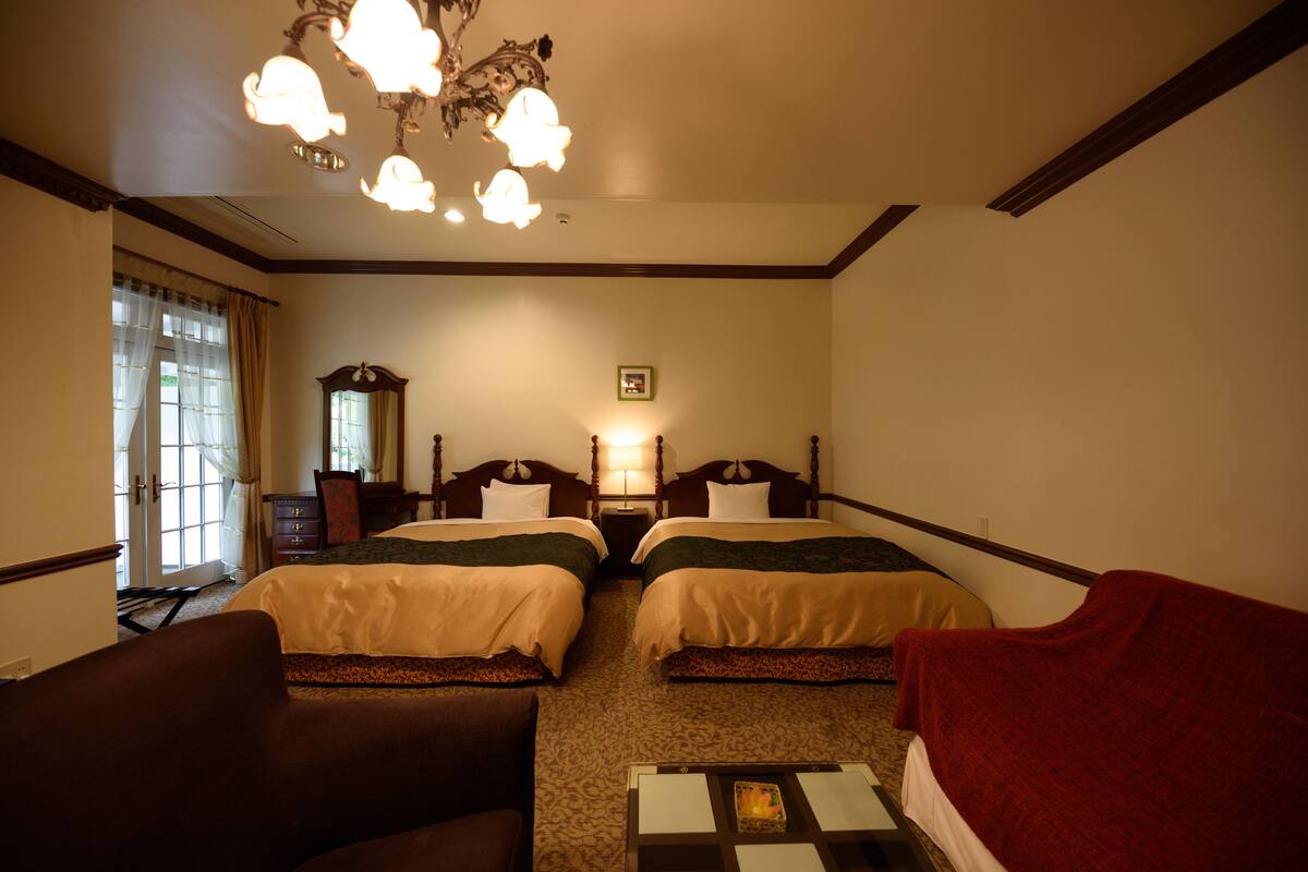 A hotel room with two beds, a desk, a chair, a dresser, and a chandelier.