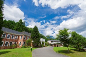 A brick building with a curved driveway, surrounded by lush greenery and trees. - Yufuin Hotel Morino Terrace (Yufu)