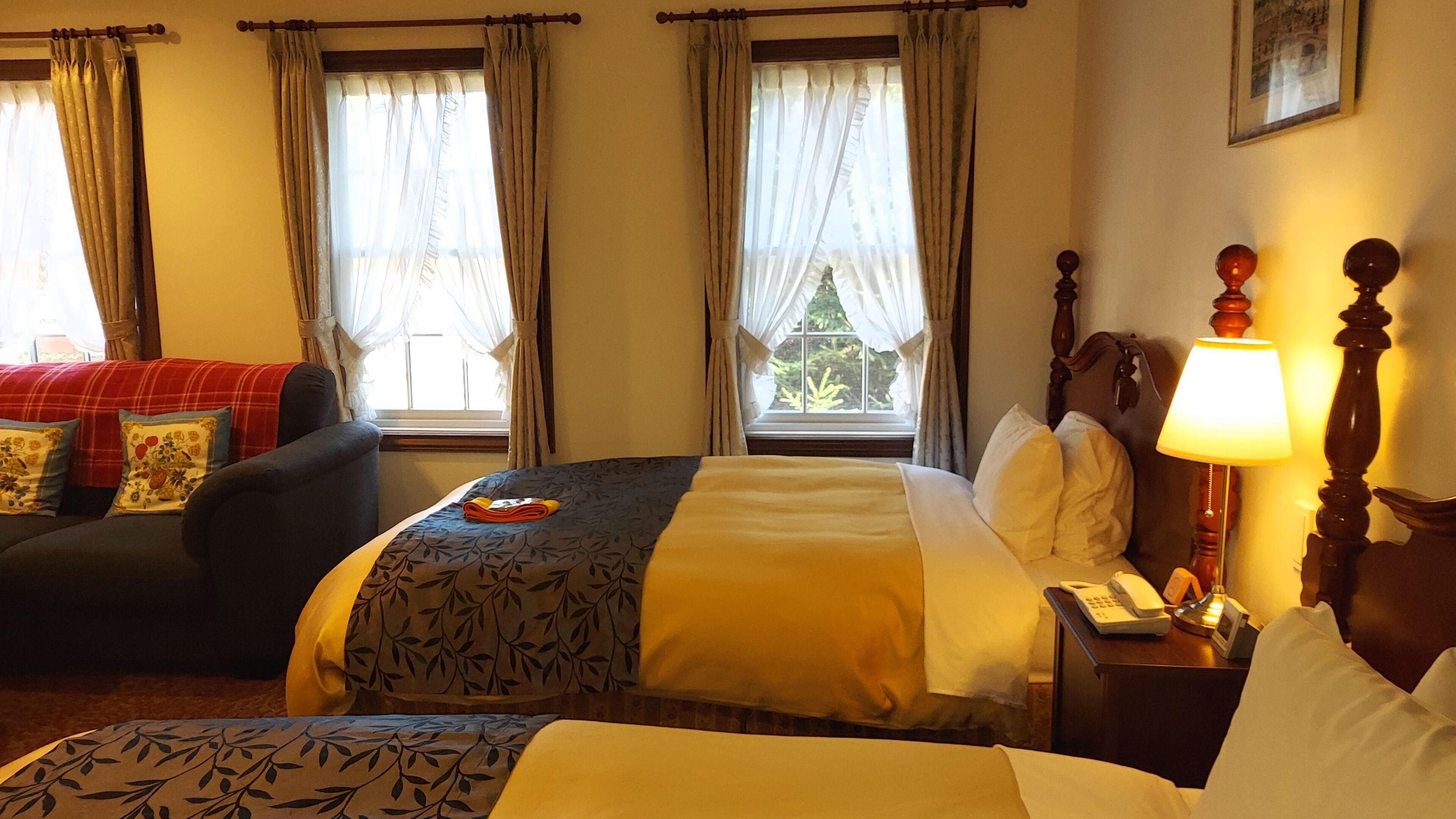 A hotel room with a bed, a chair, a bedside table with a lamp, and curtains on the windows.