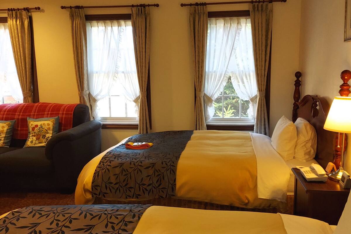 A hotel room with a bed, a chair, a bedside table with a lamp, and curtains on the windows.