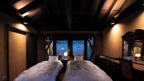 A room with two beds, a desk, and a mirror. There are windows with curtains, and the room has wooden beams on the ceiling. - Yufuin Hotel Morino Terrace (Yufu)