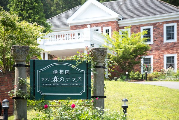 A sign for Yufuin Hotel Morino Terrace with a brick building and a white balcony in the background. - Yufuin Hotel Morino Terrace (Yufu)