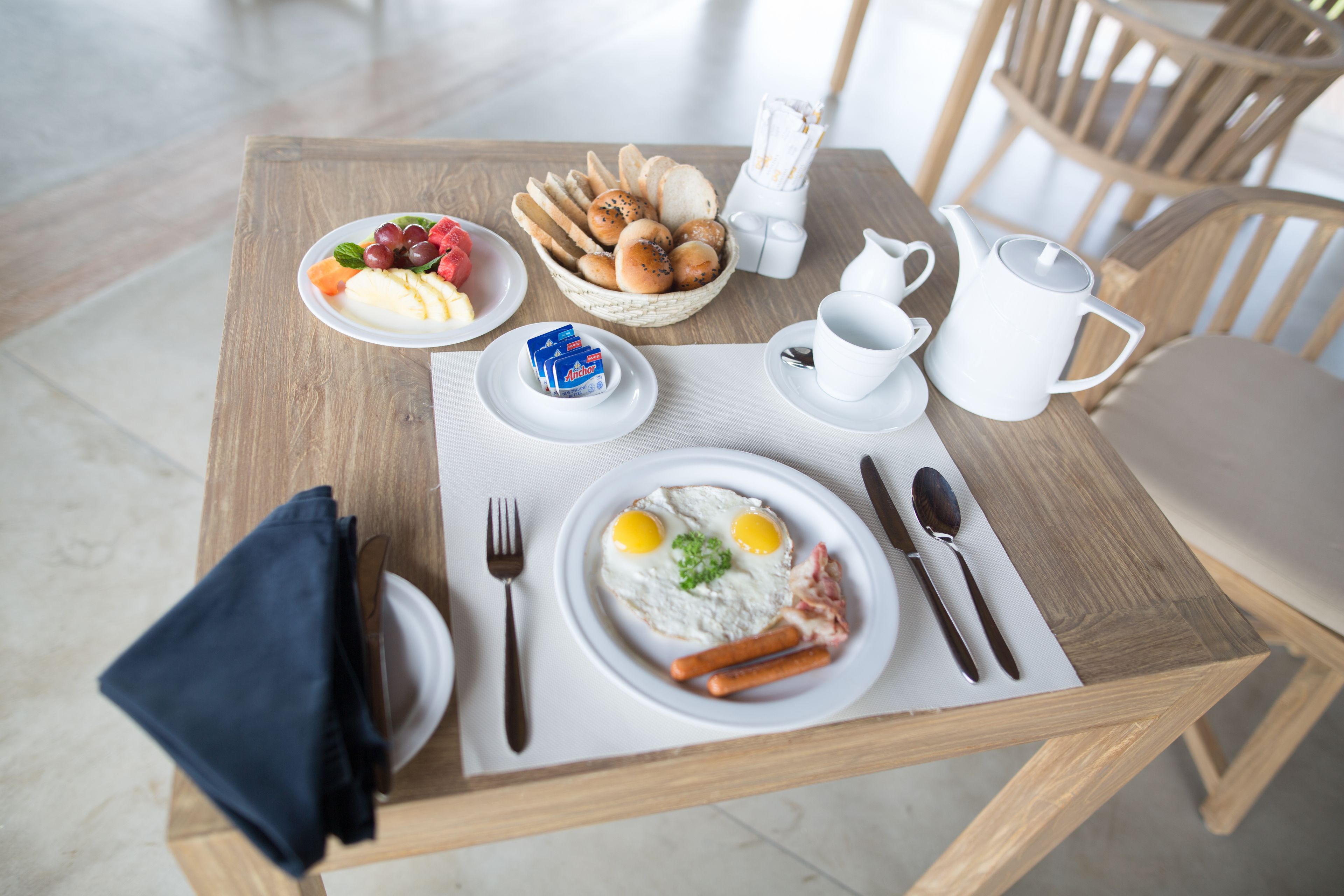 A breakfast setting with a wooden table, plates of food, and dining utensils.