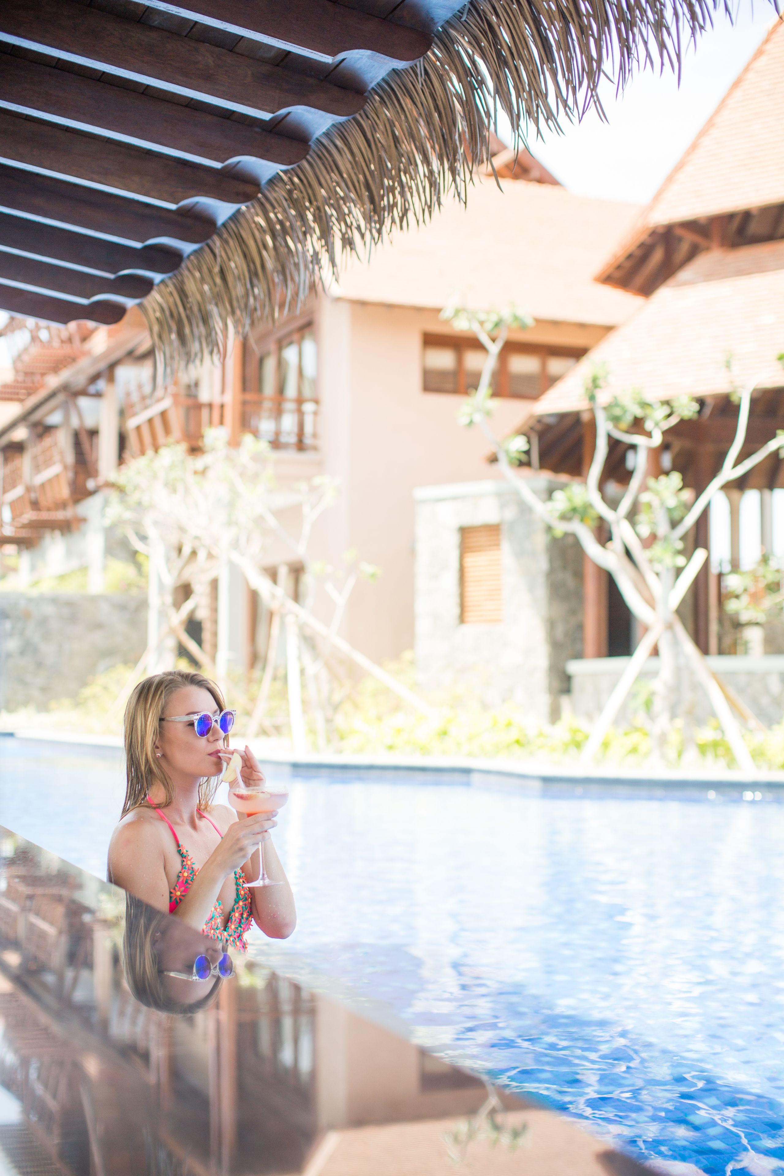 A person relaxing by a pool with a tropical setting, including wooden structures and greenery.