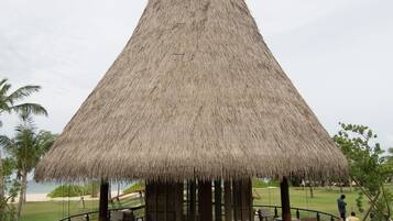 A thatched-roof structure with a wooden deck and seating area, surrounded by water.
