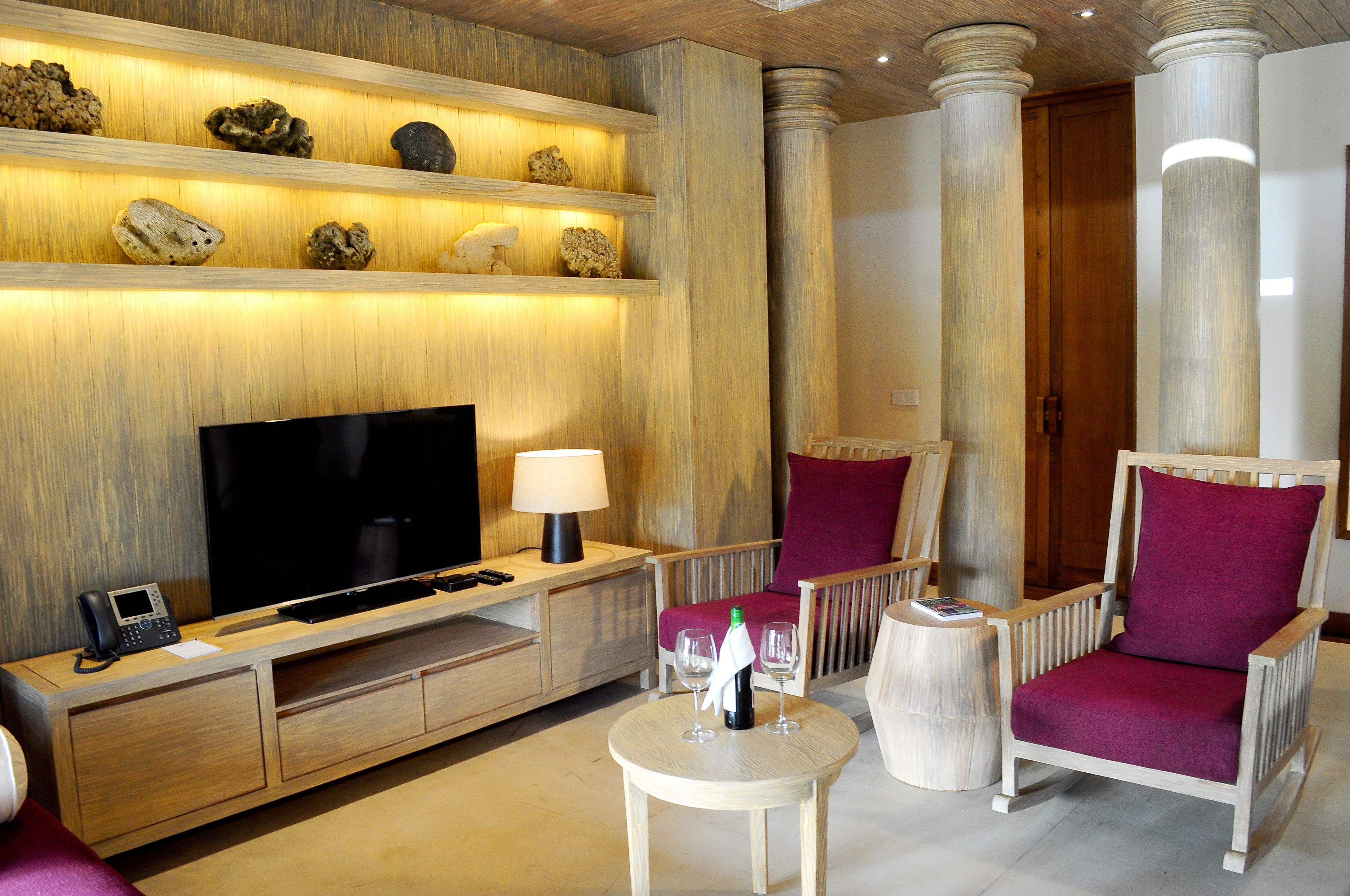 Una sala moderna con un televisor de pantalla plana, muebles de madera, una mesita redonda con una botella y vasos, y un estante con rocas decorativas.