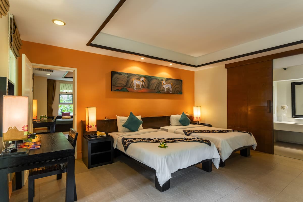 A hotel room with two beds, a desk, a chair, a nightstand, a painting, and a large mirror.