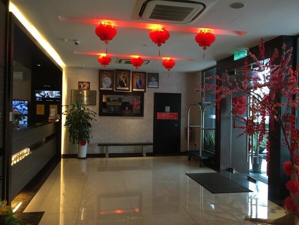 Un vestíbulo de hotel con un mostrador de recepción, un banco, una planta en maceta y faroles rojos en el techo.