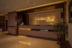 Una mesa de recepción con un cartel que dice "DELEGANCE HOTEL" y un área de recepción.