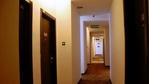 Pasillo de hotel con puertas numeradas, suelo alfombrado y un cartel que indica la dirección de la salida de incendios.