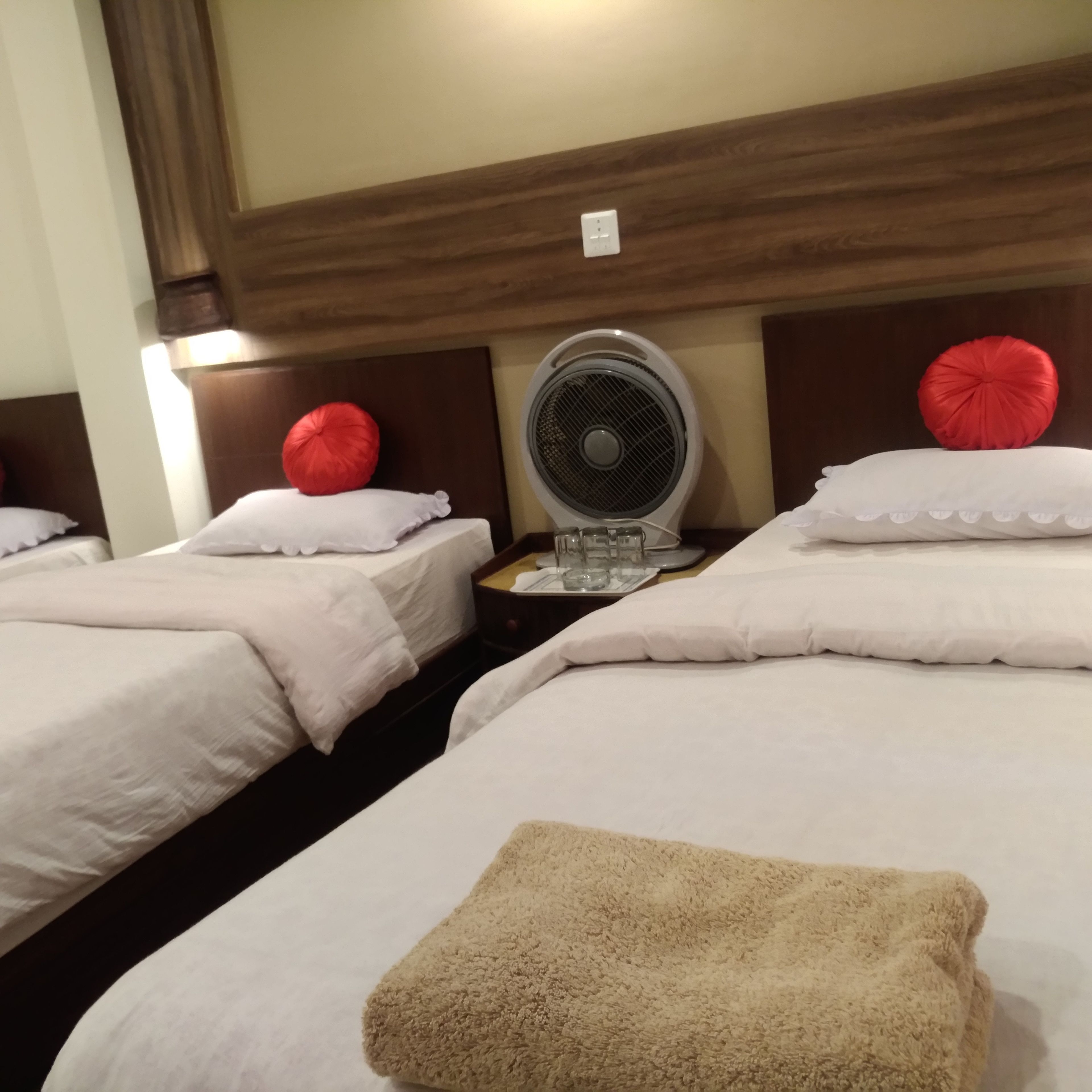 Une chambre d’hôtel avec deux lits, chacun agrémenté de draps blancs et d’oreillers décoratifs rouges. Une serviette beige est posée sur le lit, au premier plan.