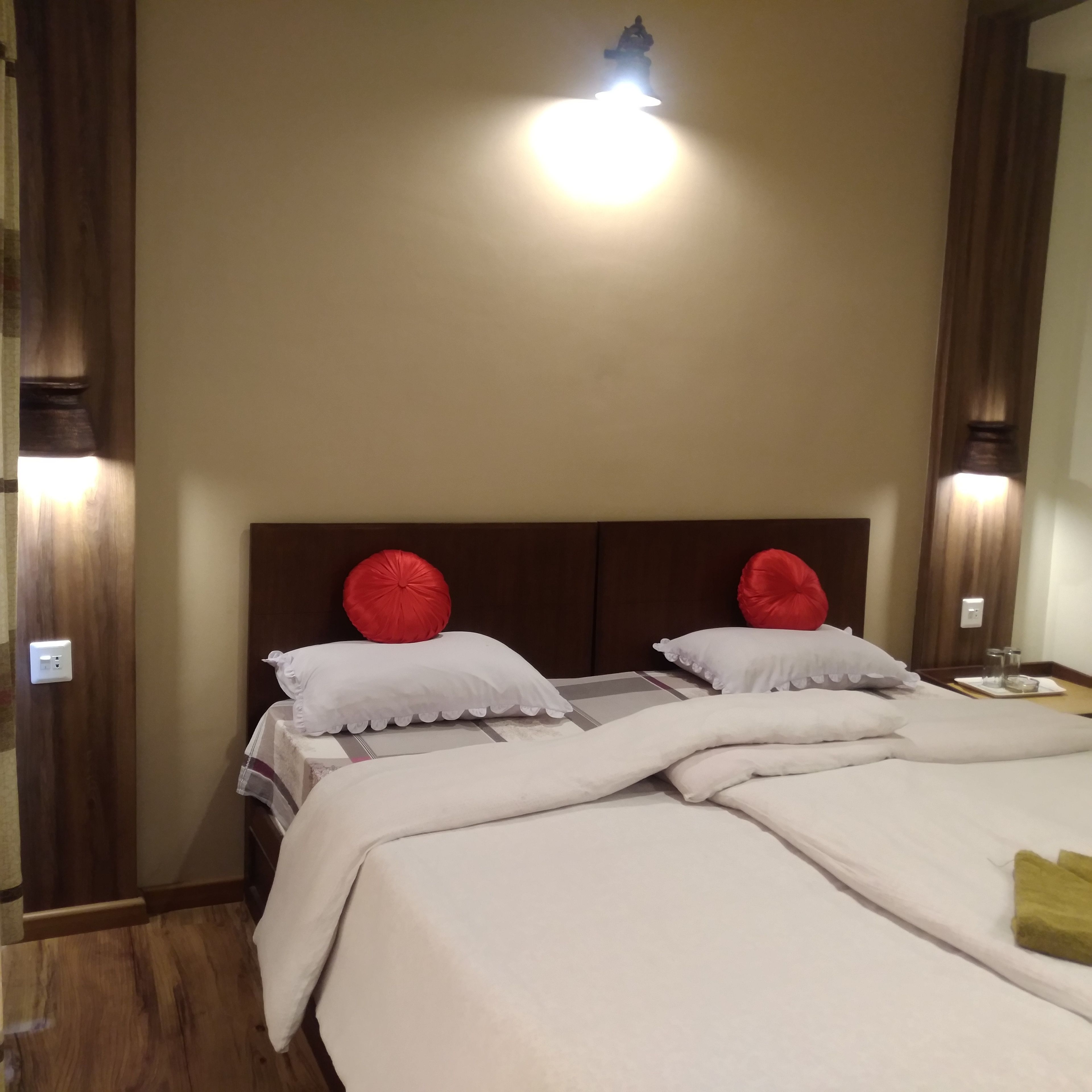 A hotel room with a wooden headboard, two red and two white pillows, a bed with white bedding, and a light fixture above the headboard.