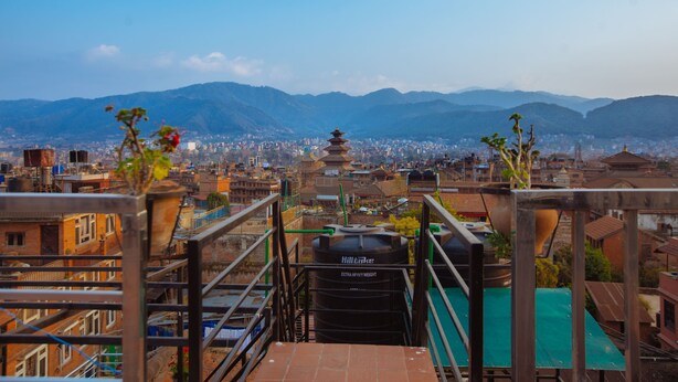 A view from a high vantage point overlooking a city with a prominent pagoda in the distance, surrounded by mountains. - Tulaja Boutique Hotel (Bhaktapur)
