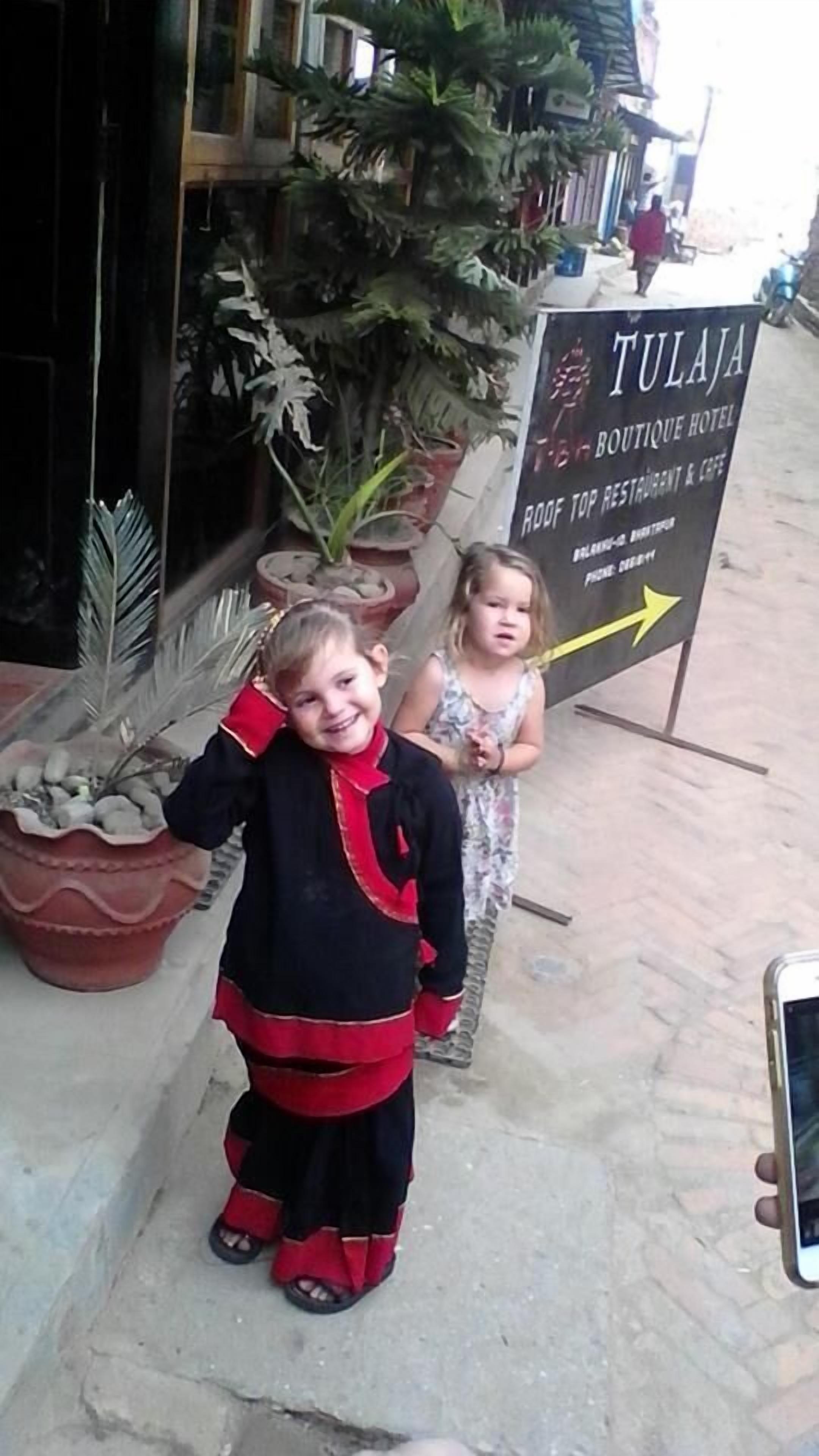 Two children standing in front of a sign for Tulaja Boutique Hotel, which advertises a roof top restaurant and cafe.
