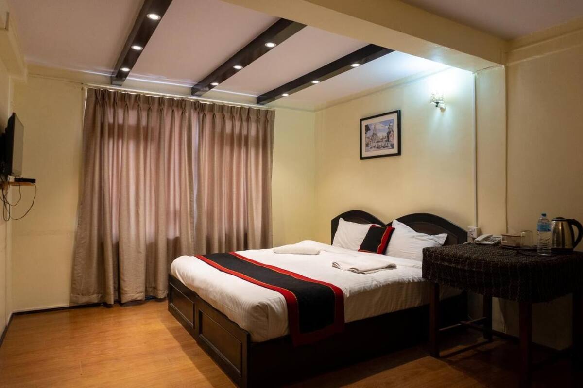Een hotelkamer met een bed, een bureau, een stoel, een schilderij aan de muur en een gordijn.