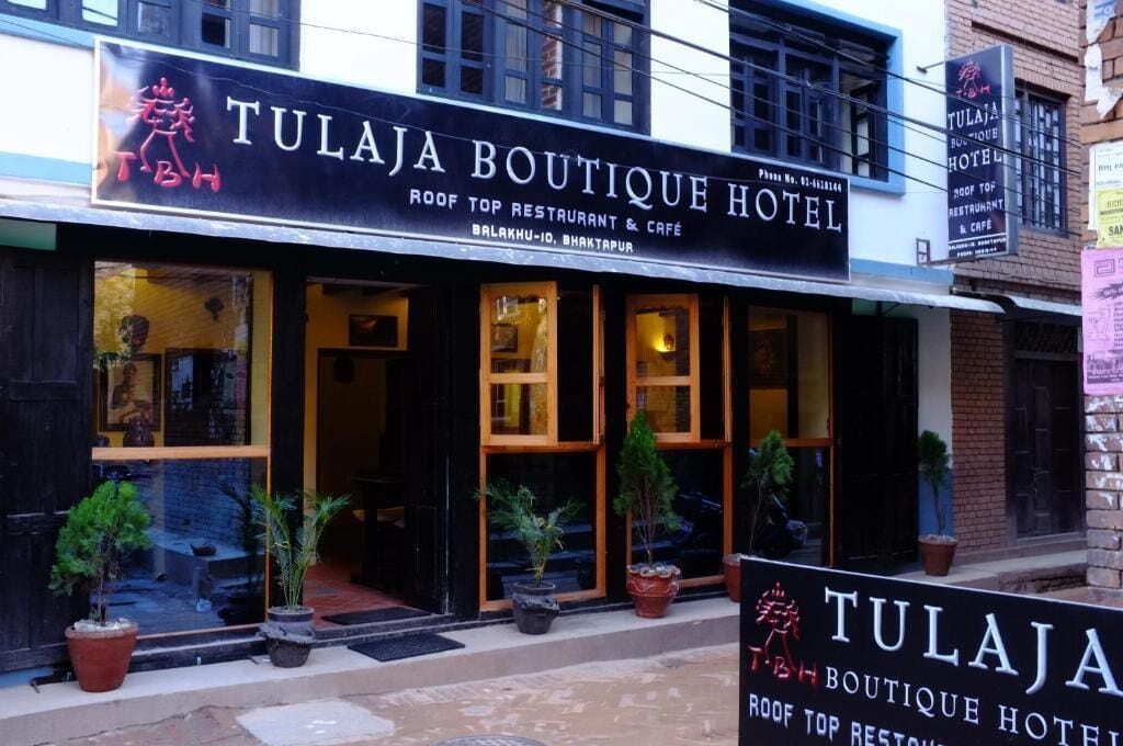 The exterior of Tulaja Boutique Hotel, featuring a black facade with large windows and potted plants in front.