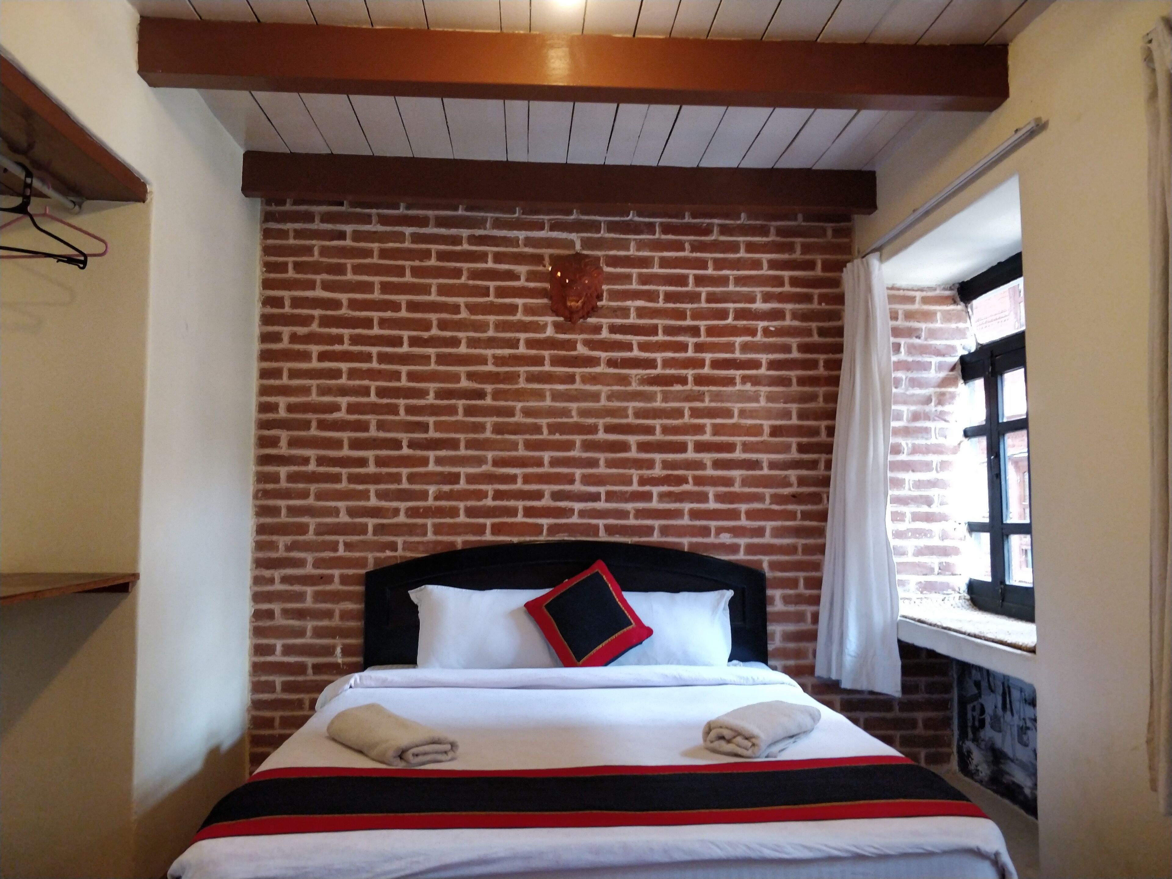 A hotel room with a brick wall, a bed with white bedding and a black headboard, and a window with curtains.