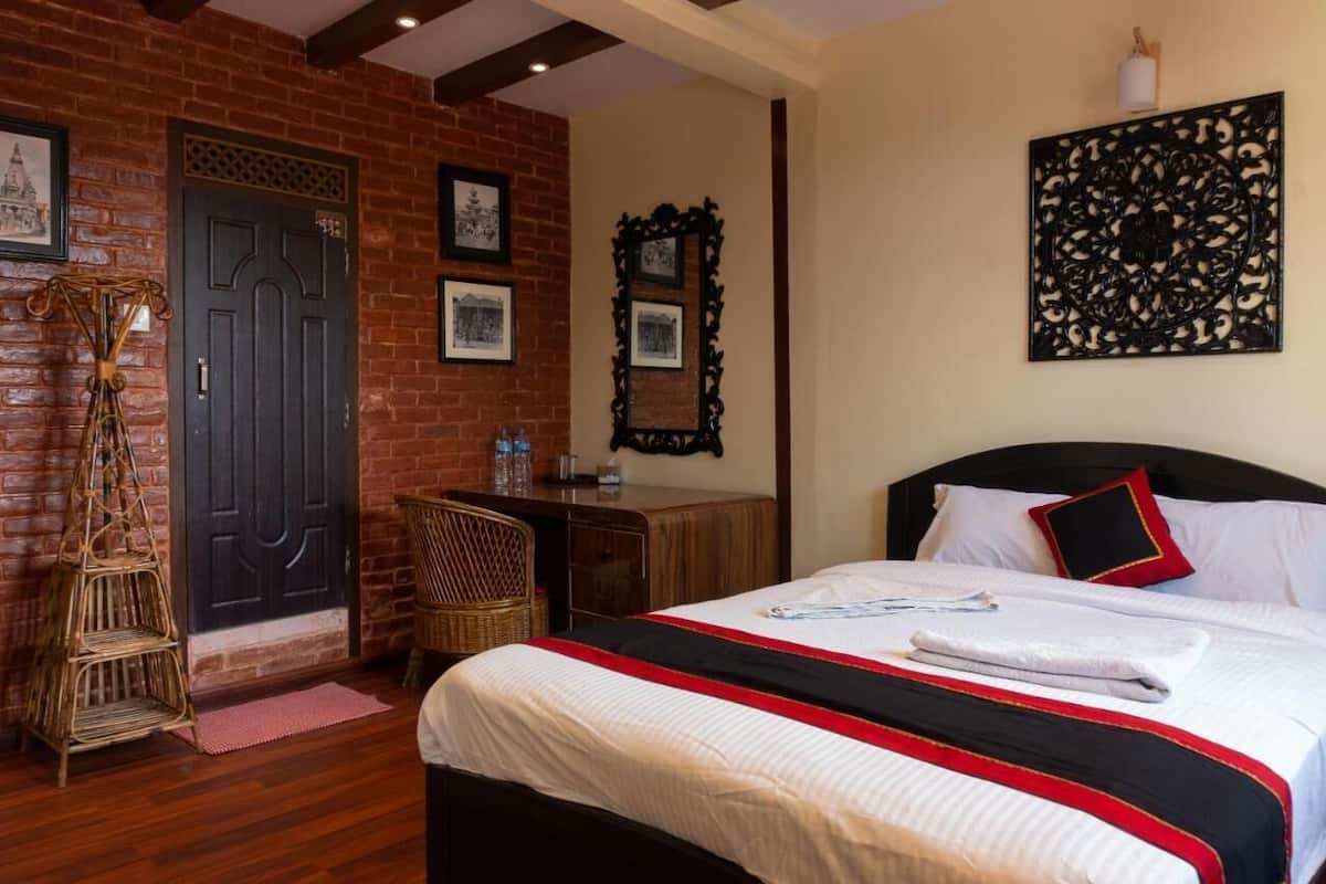 Een hotelkamer met een bakstenen muur, een bed met witte beddengoed en rode accenten, een bureau met stoel, en ingelijste foto’s aan de muur.