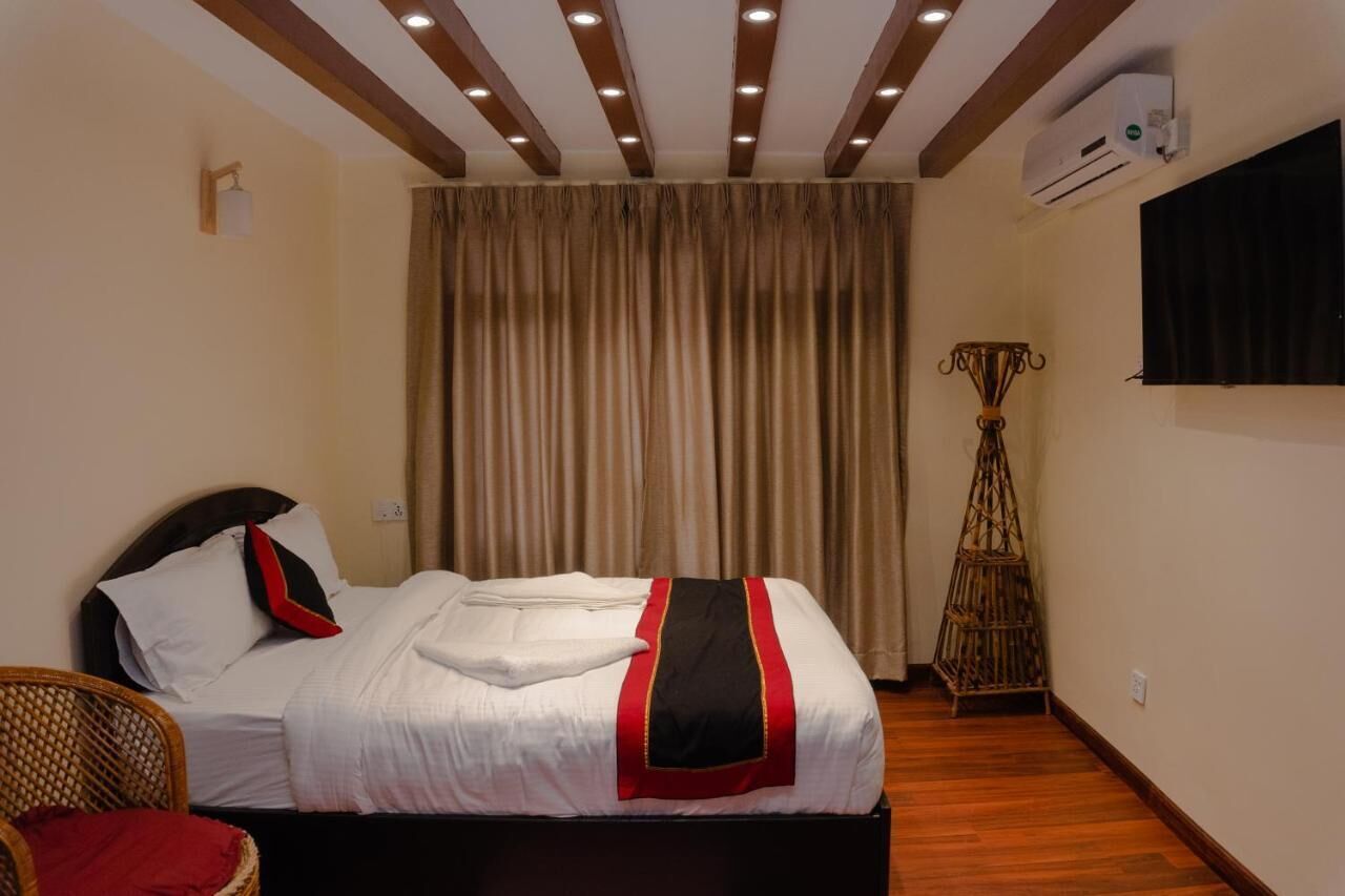 A hotel room with a bed, a chair, a wall-mounted TV, and an air conditioning unit.