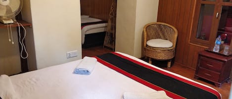 A hotel room with a bed, a chair, a fan, and a small wooden cabinet.
