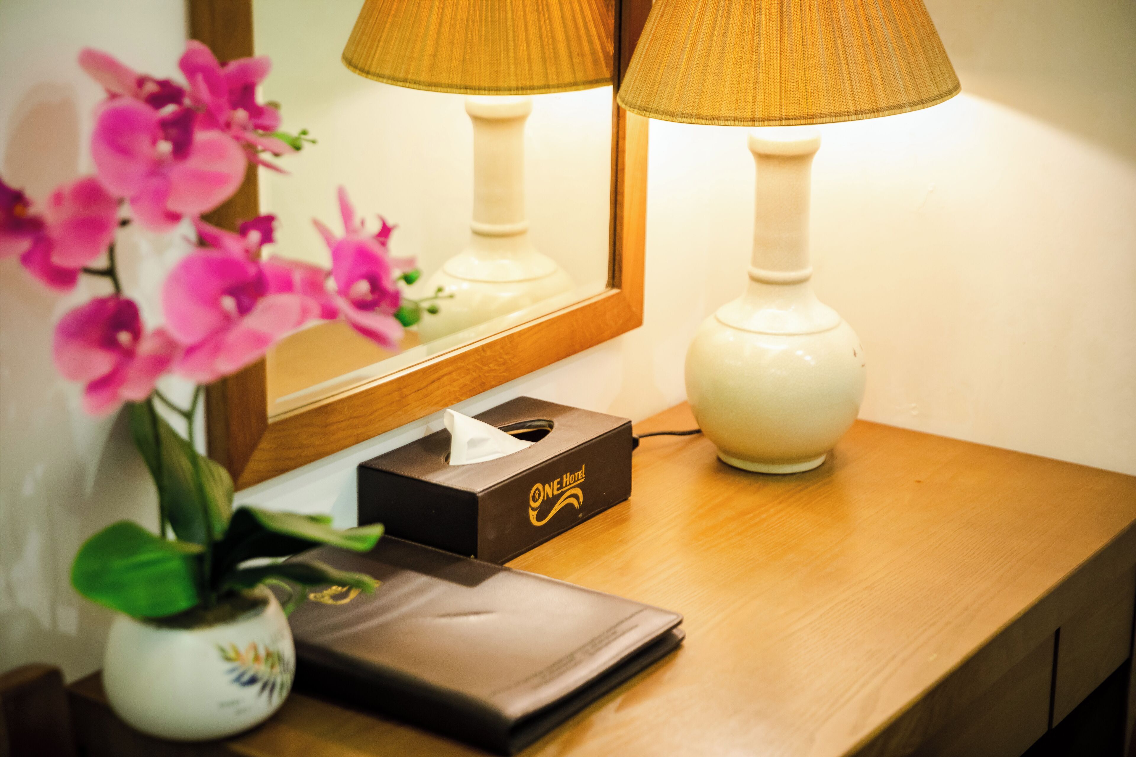 A wooden bedside table with a tissue box, a lamp, and a vase with pink flowers.