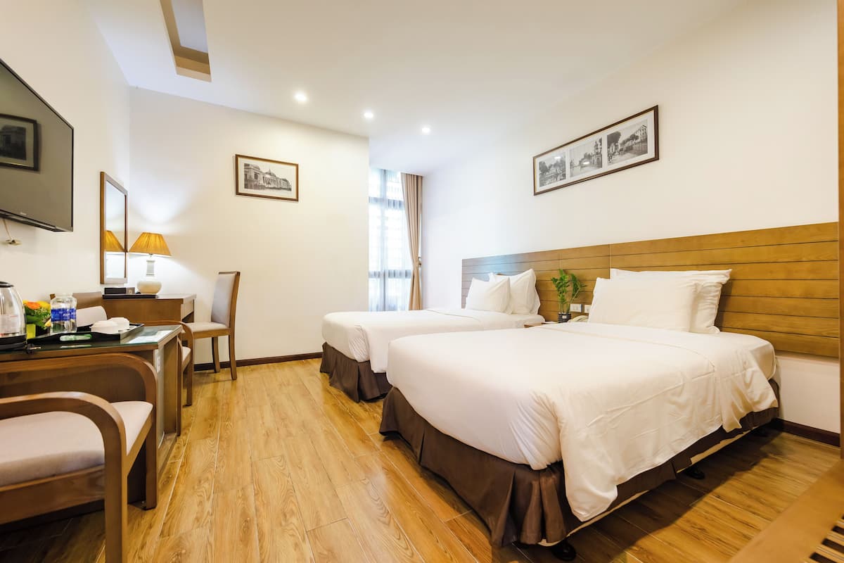 A hotel room with two beds, a desk with a lamp, a chair, and a TV.