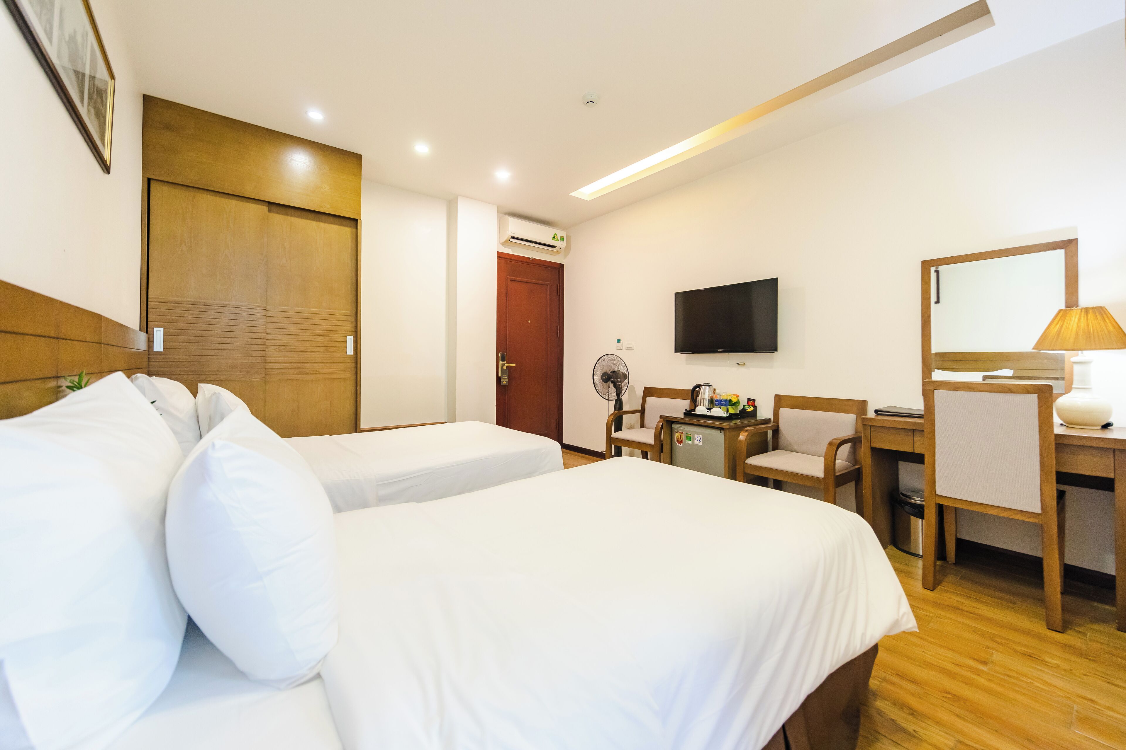 Ein Hotelzimmer mit zwei Betten, einem Schreibtisch, einem Sessel, einem Fernseher und einem Spiegel.