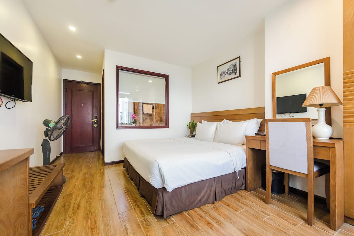 A hotel room with a bed, a desk, a chair, a TV, and a mirror.