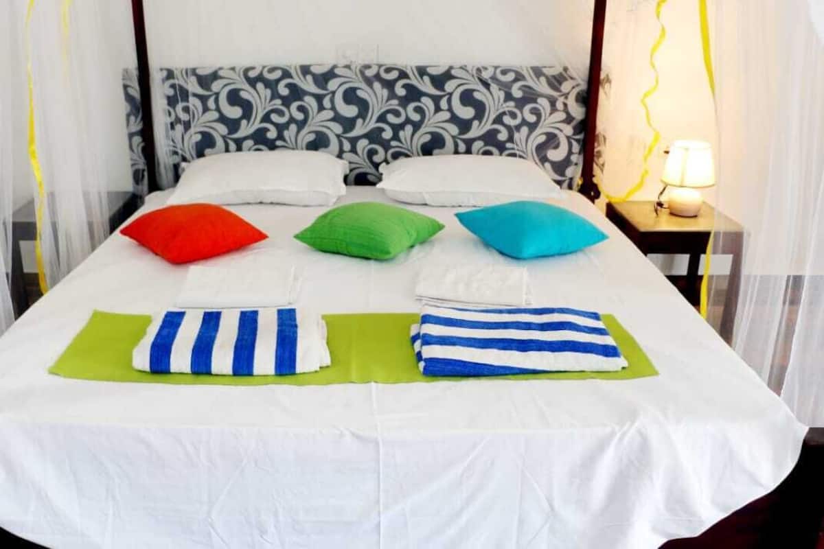 A bed with white sheets, green and blue striped towels, and colorful pillows.
