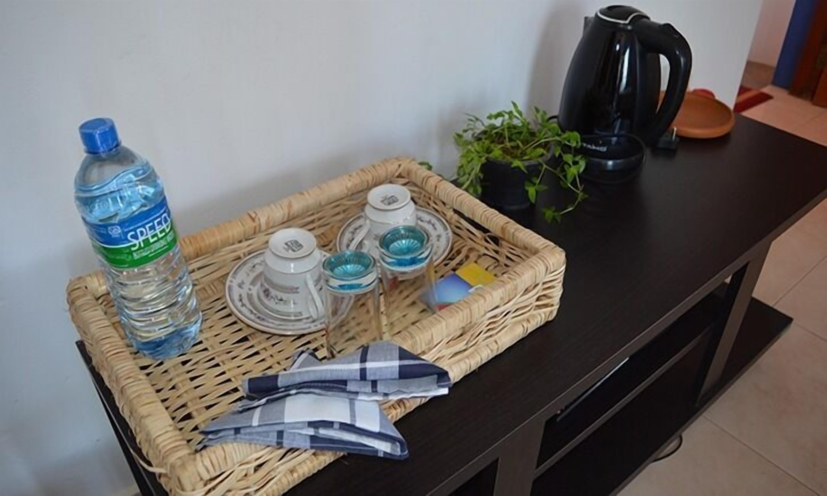 A wicker tray with a water bottle, glass containers, and a folded cloth on a dark surface.