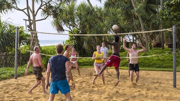A group of people playing beach volleyball on a sandy court surrounded by greenery. - Feel Beach Apartments (Kalutara)